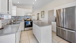 A modern kitchen with white cabinets, a stainless steel refrigerator, and a tiled backsplash. - Beautiful Direct Riverfront Paradise Home (Micco)