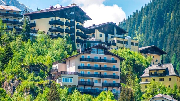 A cluster of multi-story buildings with balconies, surrounded by lush greenery and mountains in the background. - Apartment Bad Gastein Near Ski Lifts (Bad Gastein)