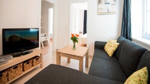 A living room with a television, a sofa, a coffee table, and a window with curtains. - Apartment Bad Gastein Near Ski Lifts (Bad Gastein)