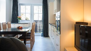 A modern kitchen with a dining area, featuring a glass table, wooden chairs, and a TV. - Apartment Bad Gastein Near Ski Lifts (Bad Gastein)