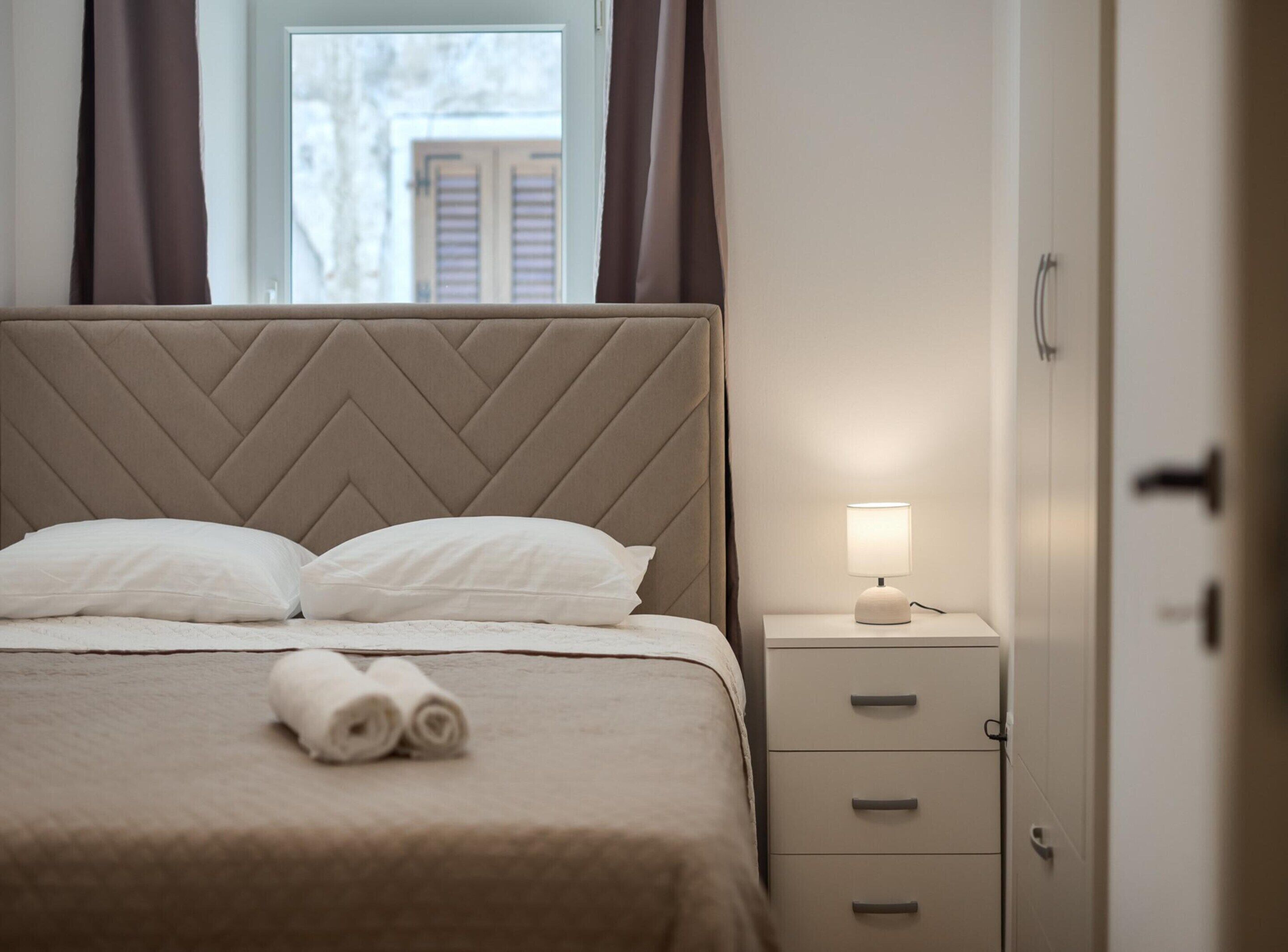 Een net opgemaakt bed met hoofdbord, een bedlampje en een aantal lades.