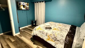 A bedroom with a bed, a television on the wall, and a door leading to another room.