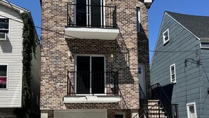 A two-story brick house with a white garage door, a small balcony on the second floor, and a visible staircase leading to the entrance.