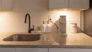 A kitchen with a stainless steel sink, white cabinets, a coffee maker, and a coffee container. - Chic 1-bedroom with AC and WiFi in downtown Newnan (Newnan)