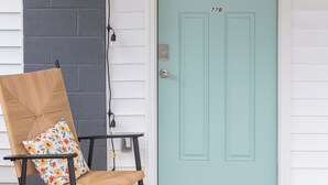 A teal door with a window above it, a rocking chair with a floral cushion, and a welcome mat on the porch. - Chic 1-bedroom with AC and WiFi in downtown Newnan (Newnan)