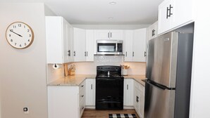 A modern kitchen with white cabinets, a stainless steel refrigerator, a microwave, and a black stove. - Chic 1-bedroom with AC and WiFi in downtown Newnan (Newnan)