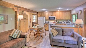 A compact living space with a kitchenette, wooden cabinets, a dining table, two sofas, and a TV.