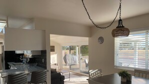 Una cocina moderna con comedor, que cuenta con un amplio ventanal con persianas, una lámpara colgante y un reloj en la pared.