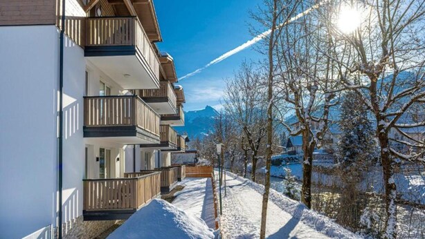 Eine Reihe moderner mehrstöckiger Gebäude mit Balkonen, vor einer verschneiten Landschaft mit Bergen im Hintergrund.