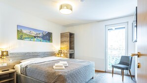 Ein modernes Schlafzimmer mit einem großen Bett, Nachttischlampen, einem Gemälde und Blick durch eine Schiebetür.