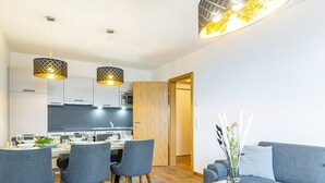 Ein modernes Wohnzimmer mit einem grauen Sofa, einem Holztisch und einem Essbereich mit grauen Stühlen und einem weißen Tisch.