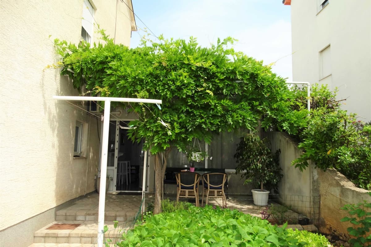 Ein überdachter Patio-Bereich mit Tisch und Stühlen, umgeben von üppigem Grün und einer weißen Pergola.