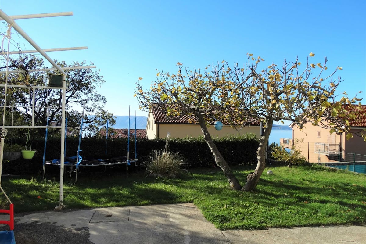 Ein Garten mit Trampolin, Schaukel und einem Baum mit gelben Blättern.