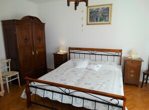 A bedroom with a wooden bed frame, a nightstand with a lamp, a wardrobe, and a painting on the wall. - Spacious Novi Vinodolski Apartments With Terrace and Shared Pool (Novi Vinodolski)