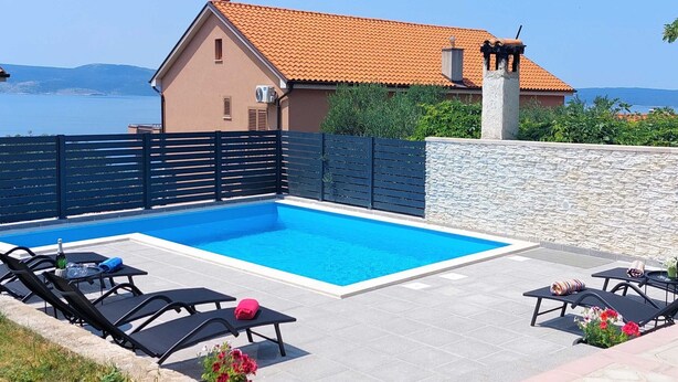 A swimming pool with lounge chairs, a stone wall, and a view of the sea. - Spacious Novi Vinodolski Apartments With Terrace and Shared Pool (Novi Vinodolski)