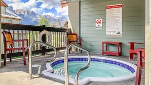 Un espace extérieur avec un jacuzzi offrant une vue sur les montagnes, un panneau indiquant qu'il est interdit de fumer et un panneau indiquant les heures d'ouverture de la piscine.