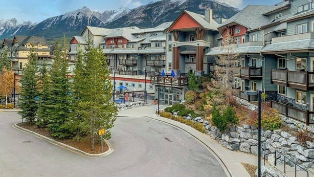 Un complexe hôtelier comprenant plusieurs bâtiments, un parking et situé au pied d’une montagne.