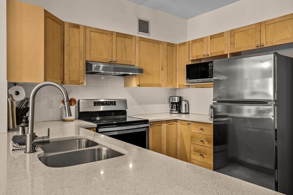 A modern kitchen with wooden cabinets, stainless steel appliances, a sink, and a microwave.