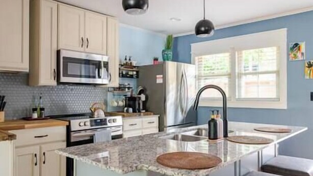 Une cuisine moderne dotée d’un îlot central, d’appareils électroménagers en acier inoxydable et de murs bleu clair.