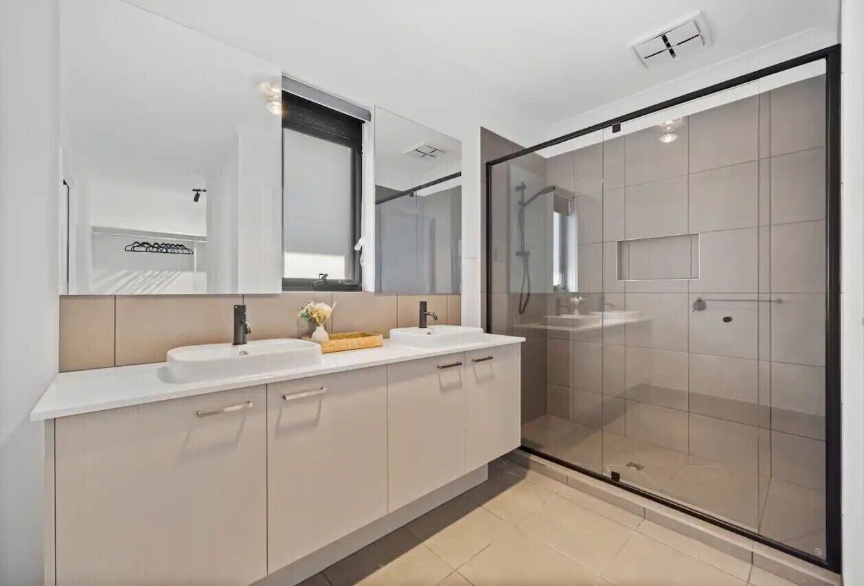 A modern bathroom with a large mirror, two sinks, a shower area, and a glass-enclosed shower.