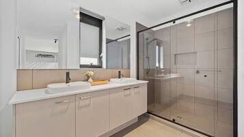 A modern bathroom with a large mirror, two sinks, a shower area, and a glass-enclosed shower.