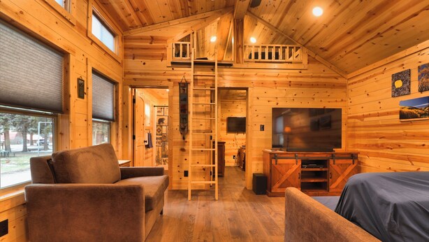 A cozy cabin interior with a loft bedroom, a TV, and a fireplace. - Golden Treasure Cabin (Red River)