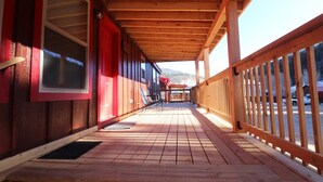 A wooden deck with a covered walkway, wooden railings, and a view of a snowy landscape. - Golden Treasure Cabin (Red River)