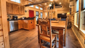 A wooden cabin interior with a kitchen, dining area, and a large window. - Golden Treasure Cabin (Red River)