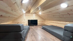 A cozy attic room with wooden walls and a sloped ceiling. It features two grey sofas and a flat-screen TV. - Golden Treasure Cabin (Red River)