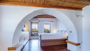Ein Schlafzimmer mit einem hölzernen Bett, weißen Wänden und einem großen, bogenförmigen Durchgang zu einem Balkon.