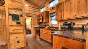 A wooden cabin interior with a kitchen area featuring granite countertops, a stove, and a coffee maker. - Booker Retreat Cabin (Red River)