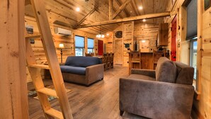A log cabin interior with a sofa, armchair, and wooden ladder. - Booker Retreat Cabin (Red River)