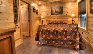 Relax in a serene bedroom with a quilted bedspread, bedside table, and framed artwork.