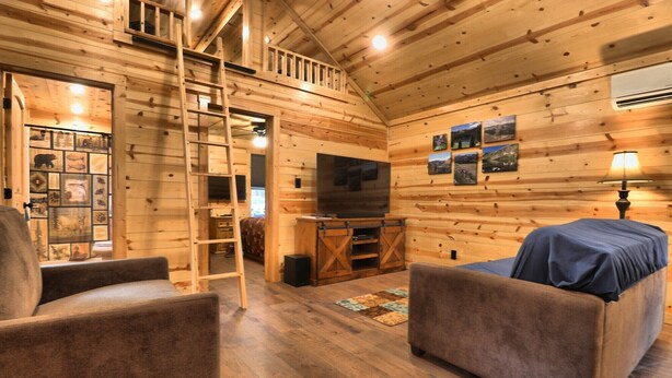 A cozy cabin interior with wooden walls, a TV, a ladder, and a sofa. - Booker Retreat Cabin (Red River)