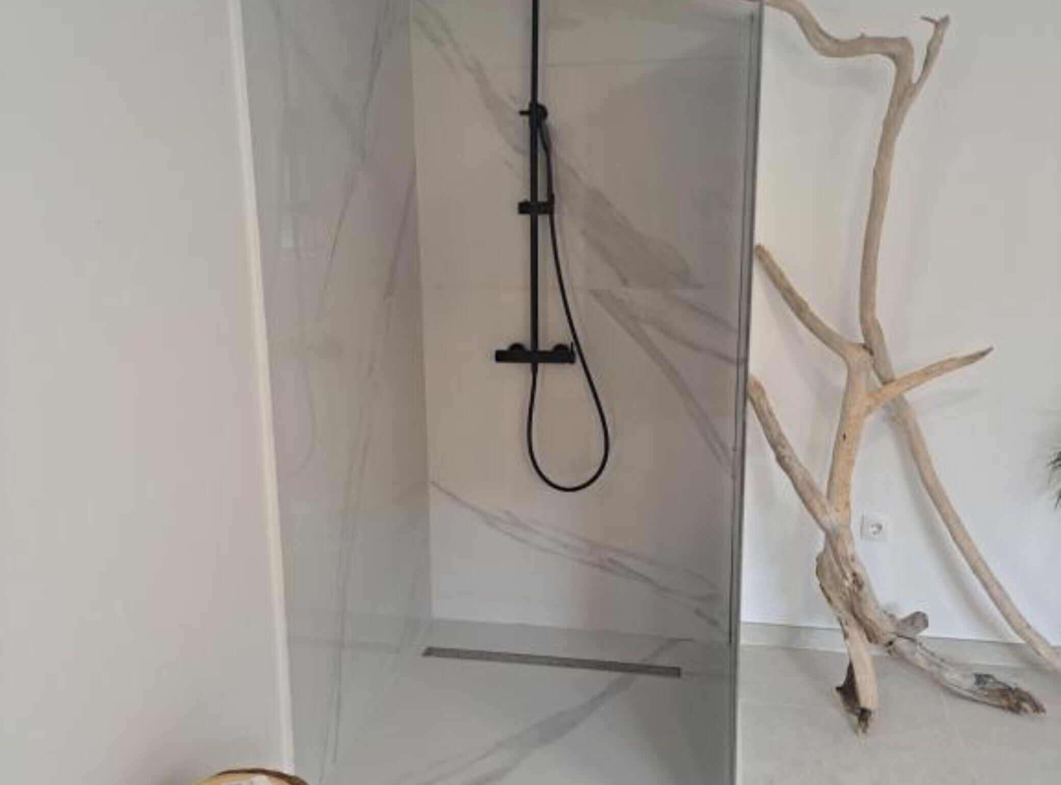 Ein modernes Duschgehäuse mit Glastür und einer Holzastdekoration auf dem Boden.