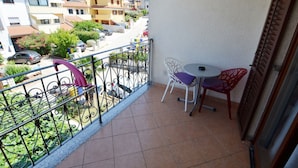 Un balcon doté d’un sol carrelé, d’une rambarde en métal et de deux chaises avec des coussins.