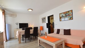 Una habitación con piso de madera, una mesa de comedor con sillas, un sofá, una mesita de centro y un cuadro en la pared.