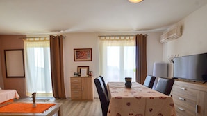 Un comedor con una mesa preparada para dos, un mueble con cajones, un televisor y un cuadro en la pared.