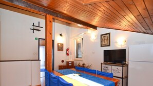 Un comedor con una mesa de madera y sillas azules, un televisor y un refrigerador.