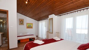 Habitación de hotel con dos camas, techo de madera, paredes blancas y un balcón con sillas.