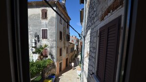 Une rue étroite, bordée de bâtiments des deux côtés, dont certains sont dotés de volets, et on peut apercevoir quelques unités de climatisation.