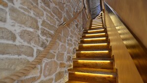 Un escalier en bois, avec des murs en pierre, menant à un niveau supérieur.