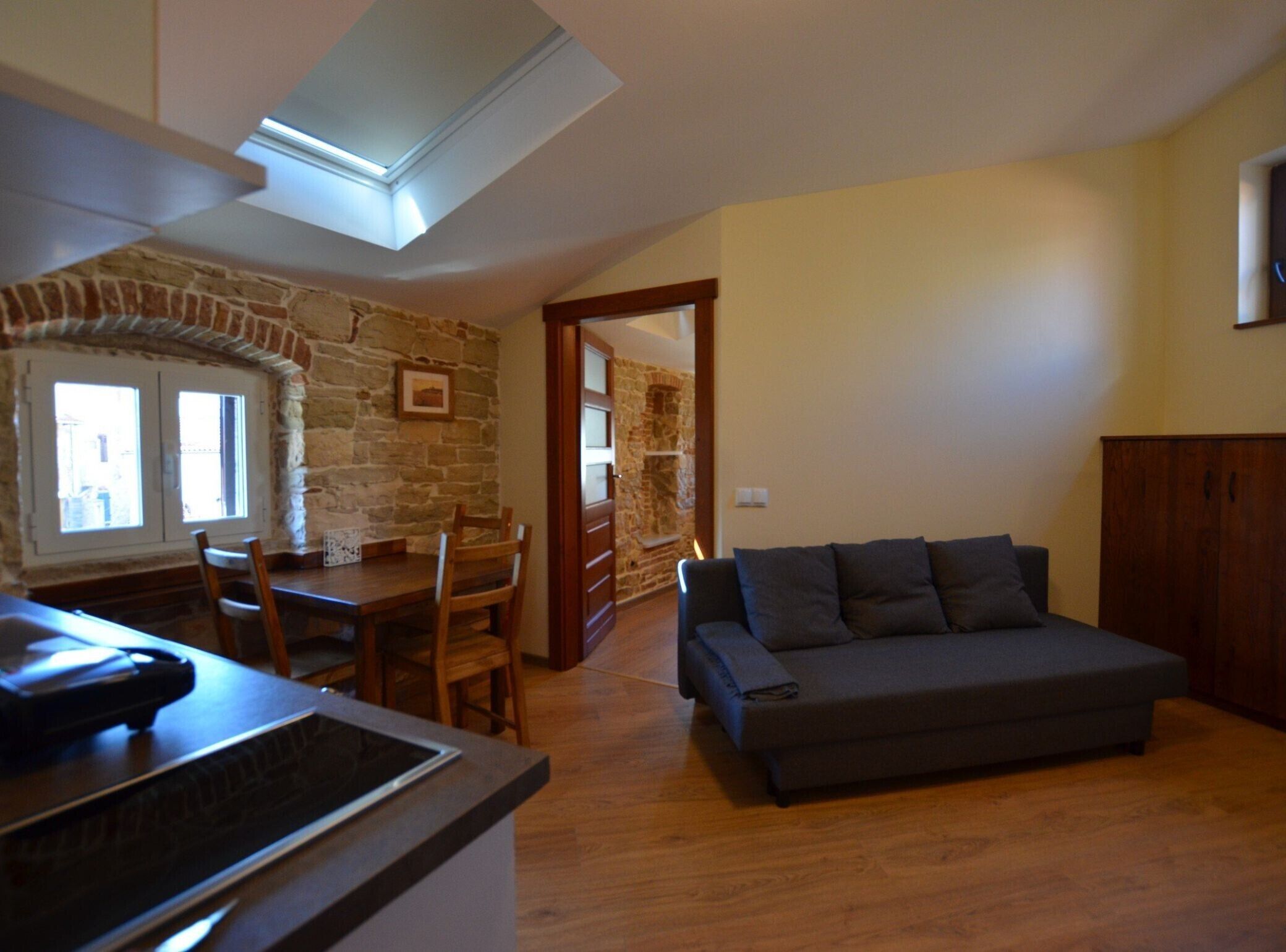 A cozy living room with a sofa, a dining table with chairs, a stone wall, and a skylight.
