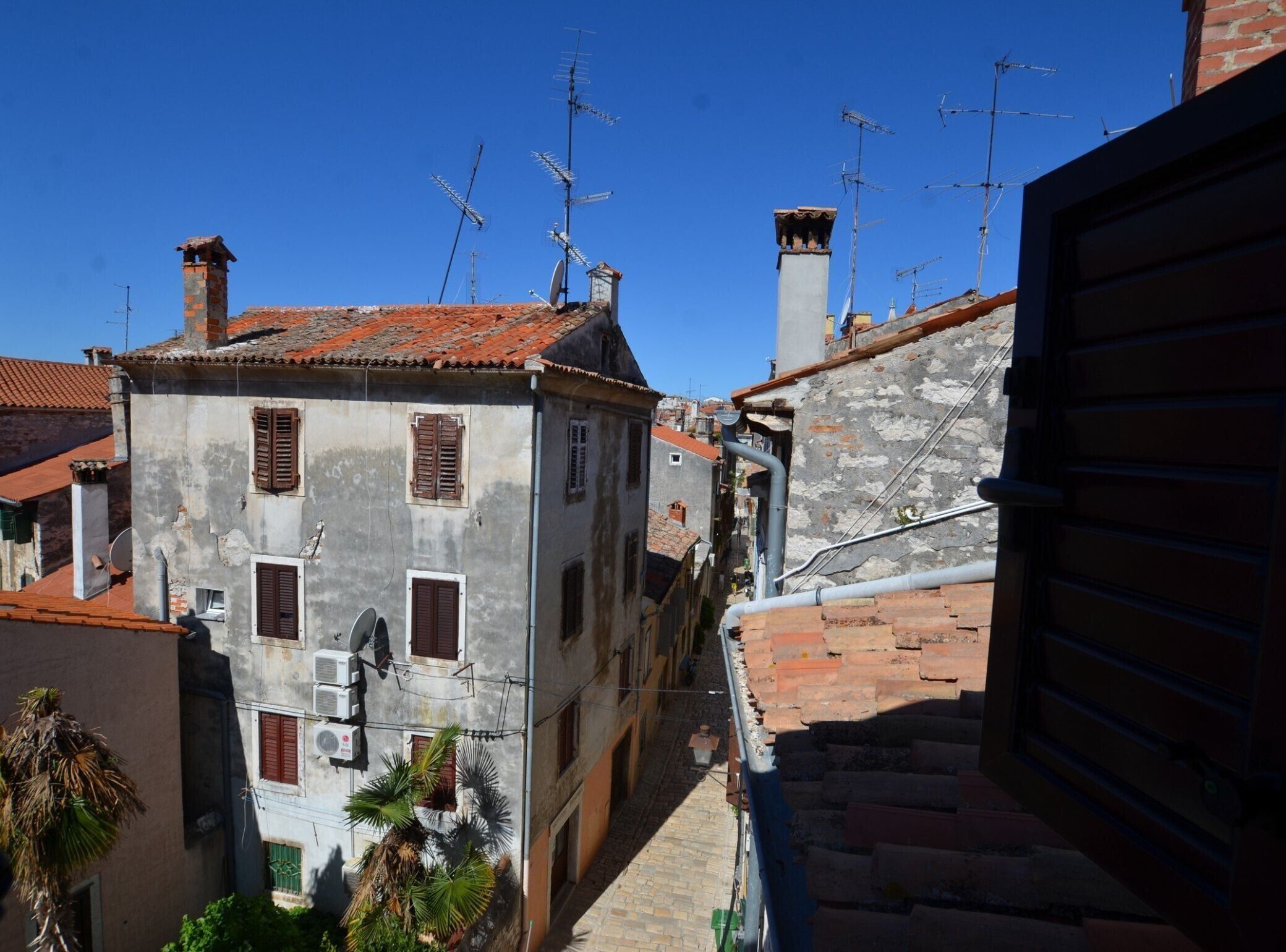 Una stretta via fiancheggiata da edifici antichi, alcuni con parabole e antenne.