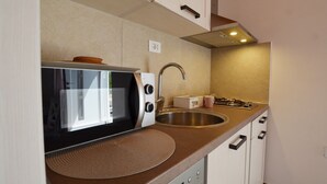 Een kleine keuken met een magnetron, spoelbak en fornuis.