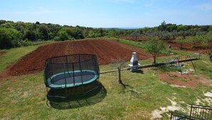 Un espacio con césped, un trampolín, una parrilla y un conjunto de columpios.