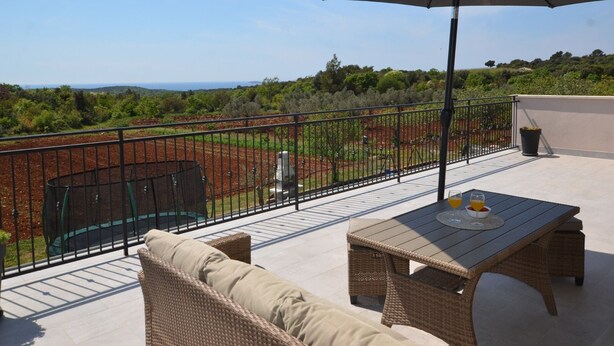 Una terraza con mobiliario de mimbre, una mesa y una sombrilla.
