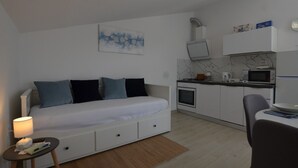 Un espacio habitable pequeño con sofá, una mesita, kitchenette y una obra de arte colgada en la pared.
