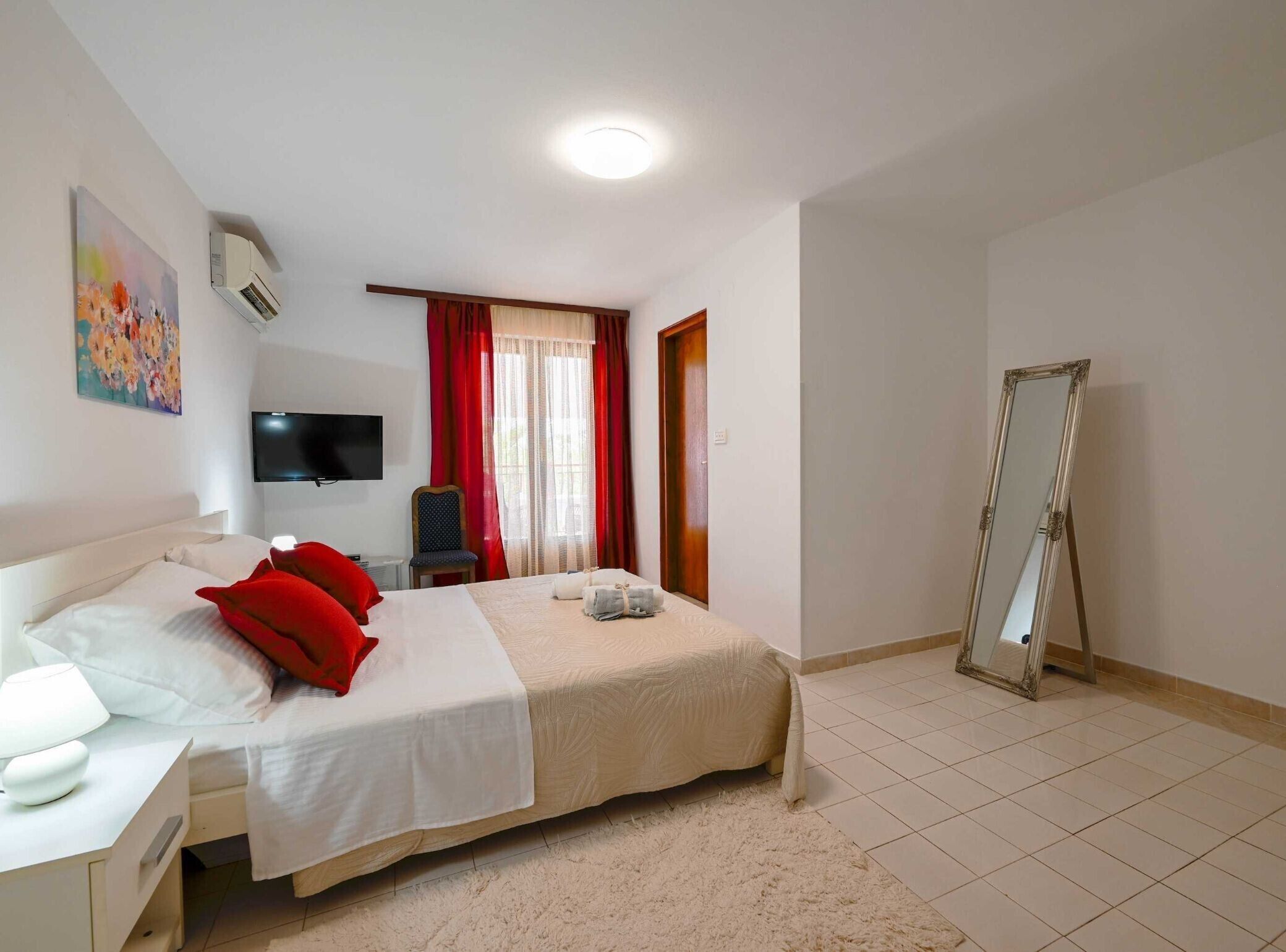 Habitación de hotel con cama, televisor, sillón, espejo y ventana con cortinas.