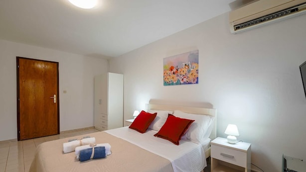 A hotel room with a bed, a nightstand, a desk, a chair, an air conditioning unit, and a door.